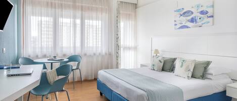 A hotel room with a bed, a desk, chairs, and a painting on the wall.