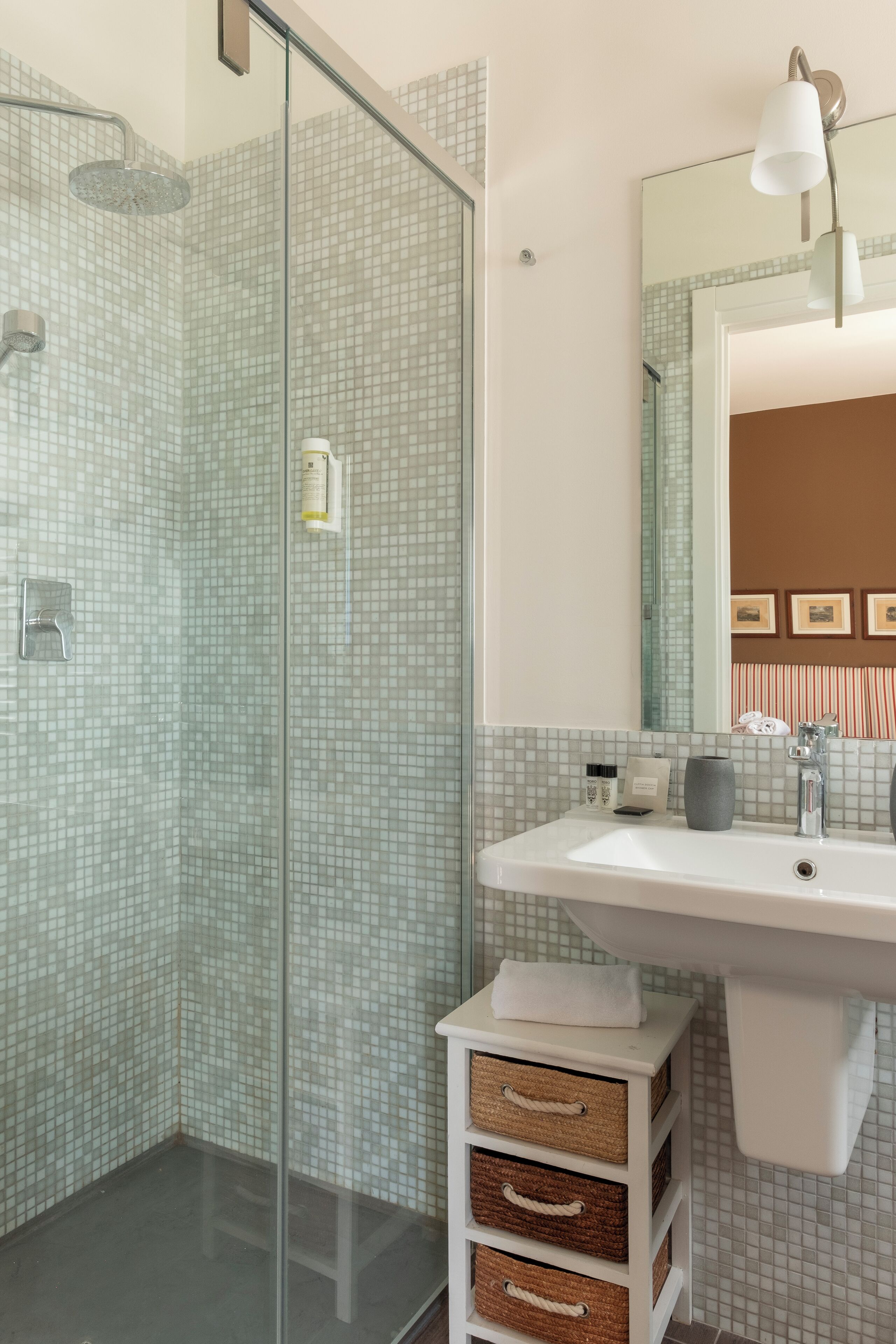 A bathroom with a glass shower enclosure, a white sink, and a mirror above it.