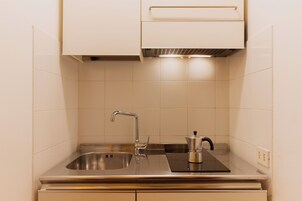 A kitchen with a stainless steel sink, a kettle, and a built-in stove.