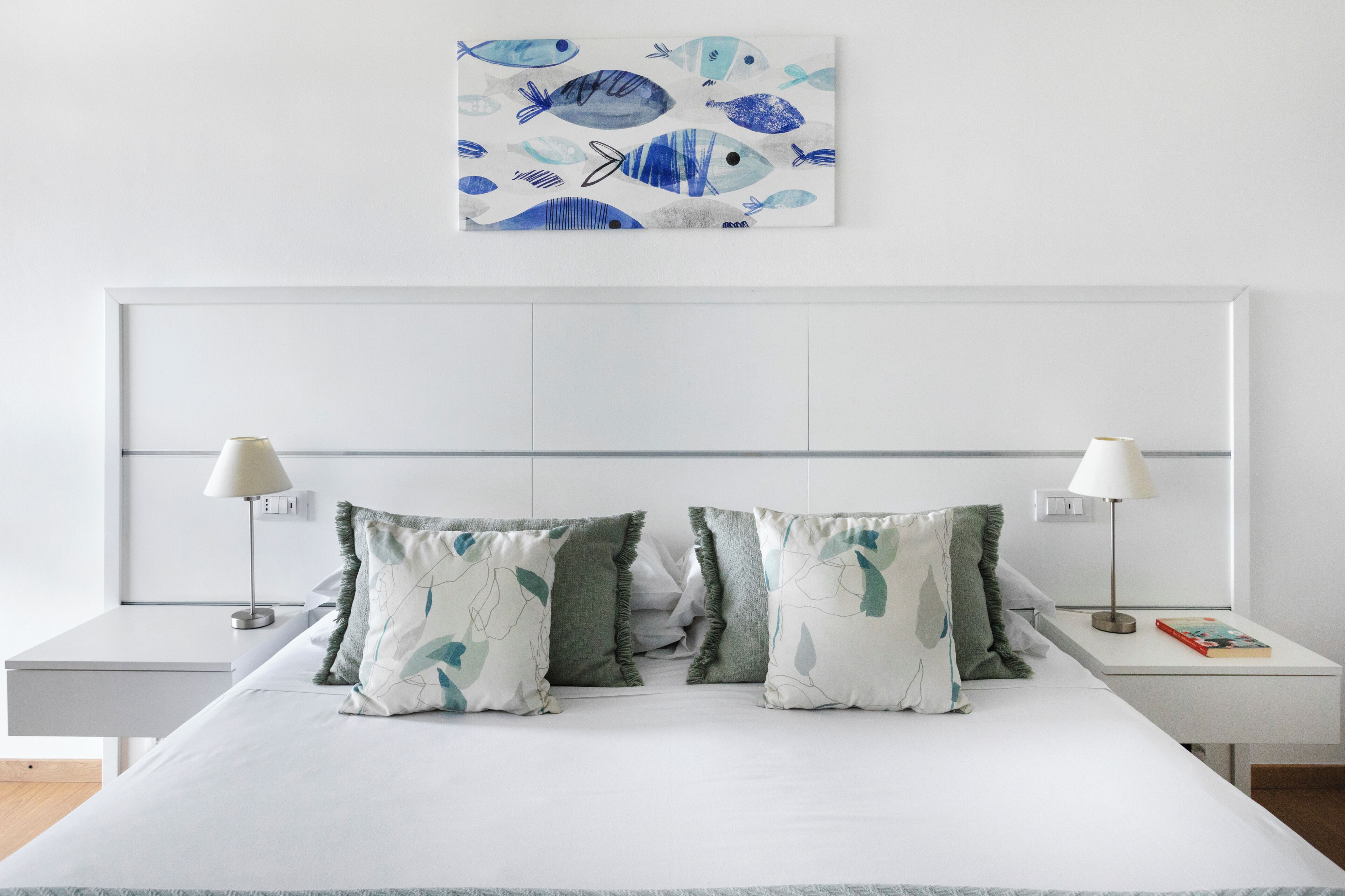 A bedroom with a bed, two bedside tables, two lamps, and a wall-mounted artwork.