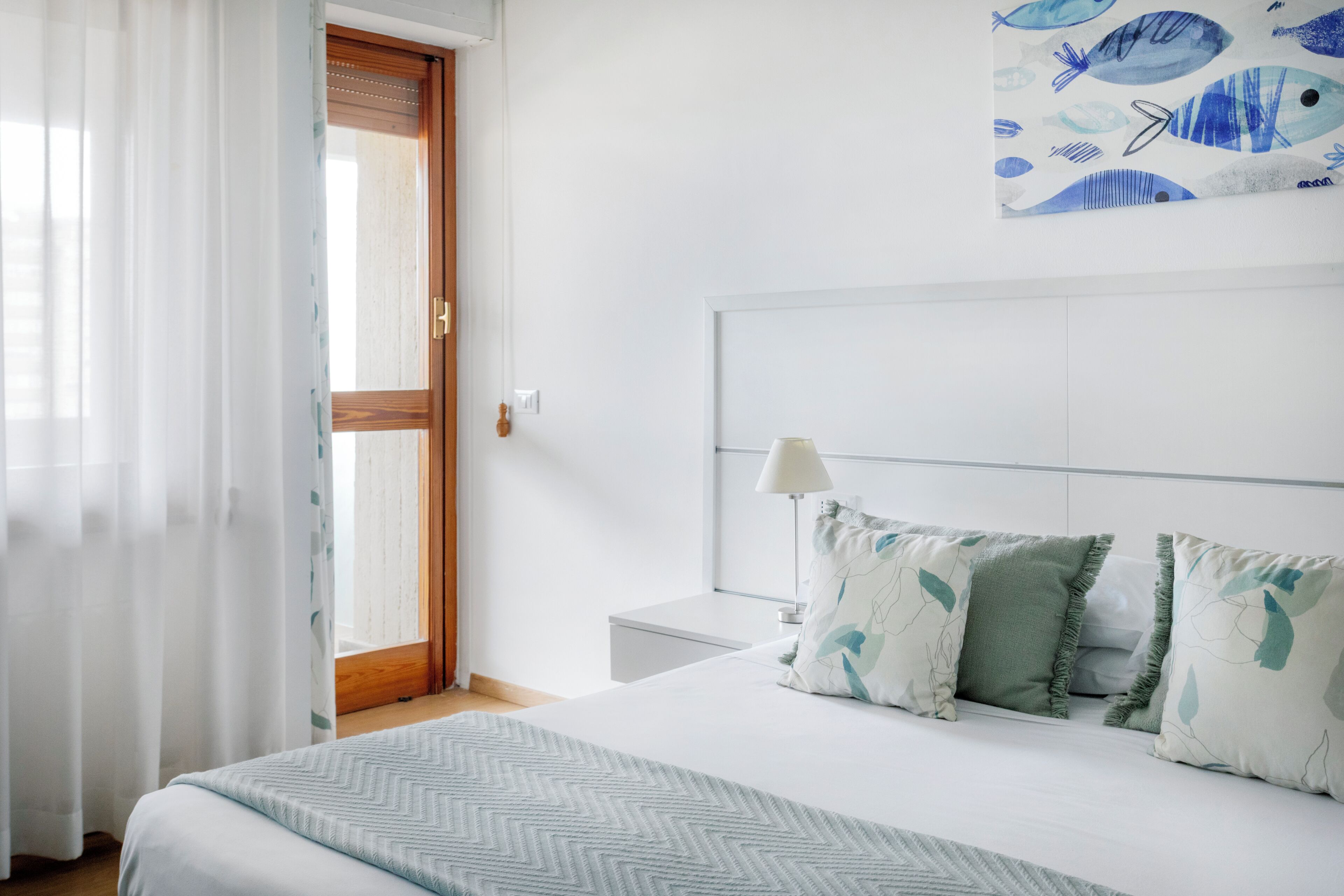 Un dormitorio con cama, mesita de noche, lámpara y ventana con cortinas.