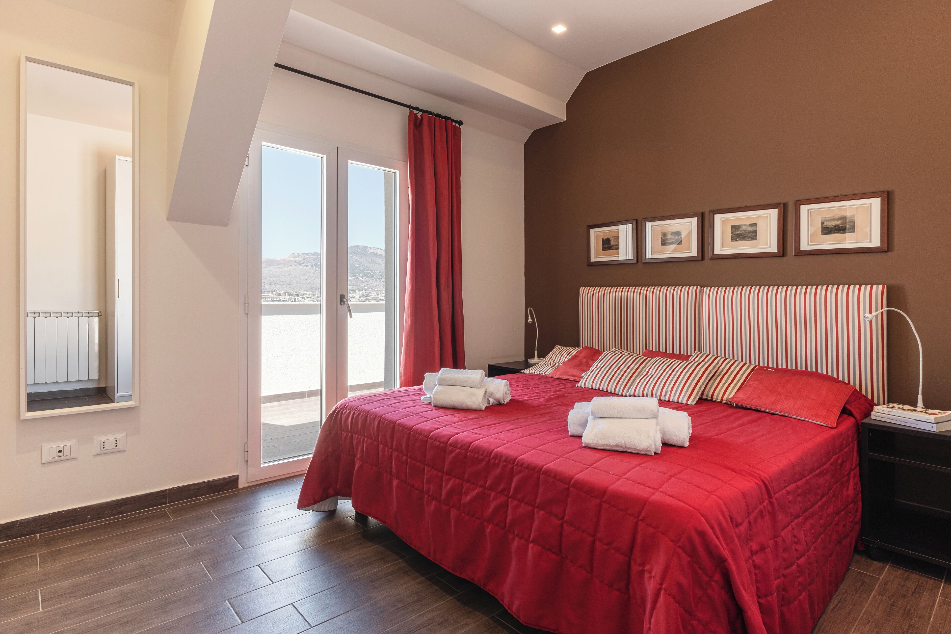 A hotel room with a large bed, a view through the sliding glass door, and a red curtain.