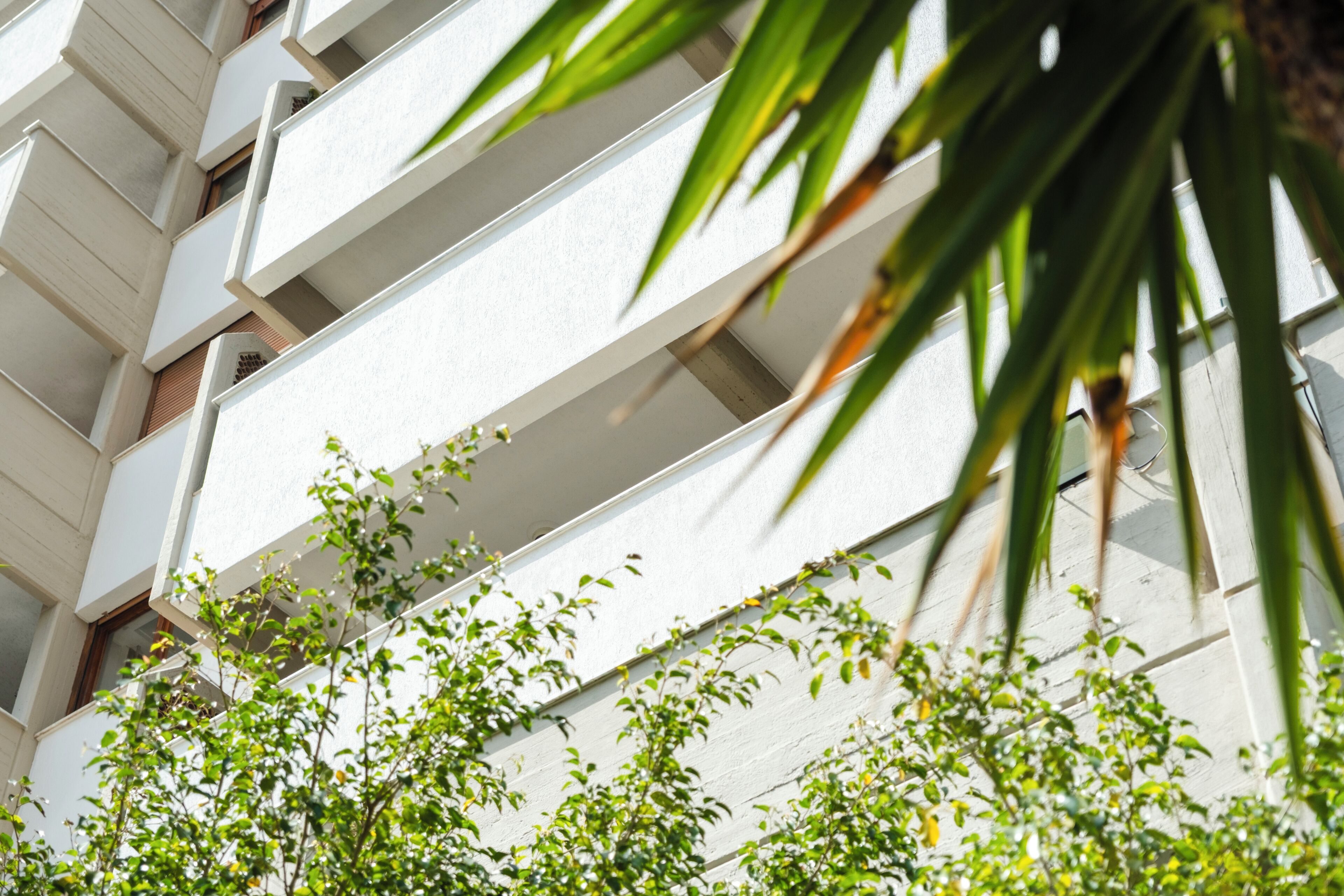 A multi-story building with balconies and greenery in front.