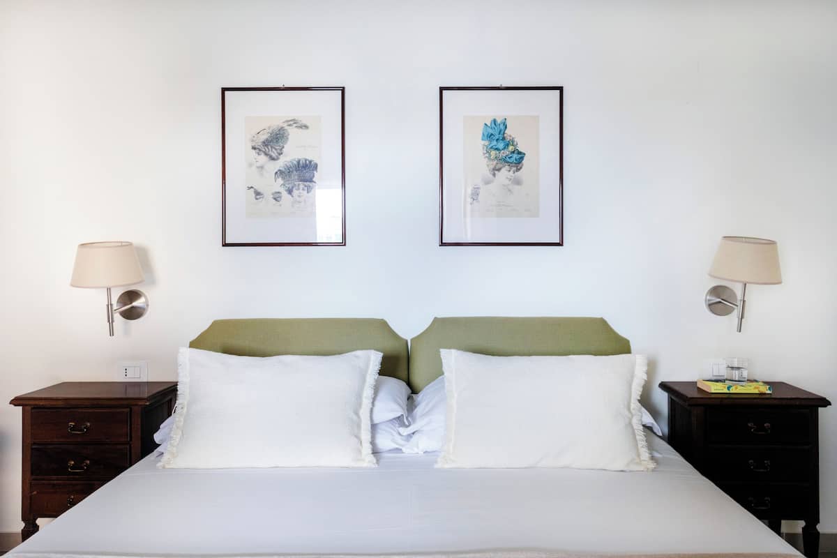 A hotel room with a double bed, two nightstands, two wall-mounted lamps, and two framed artworks on the wall.