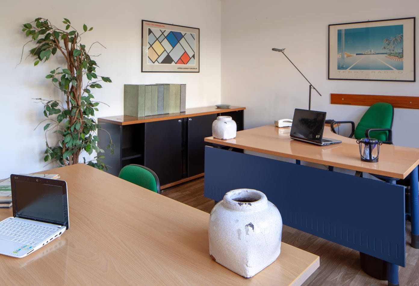 A modern office with a wooden desk, a laptop, a vase, and a green chair.