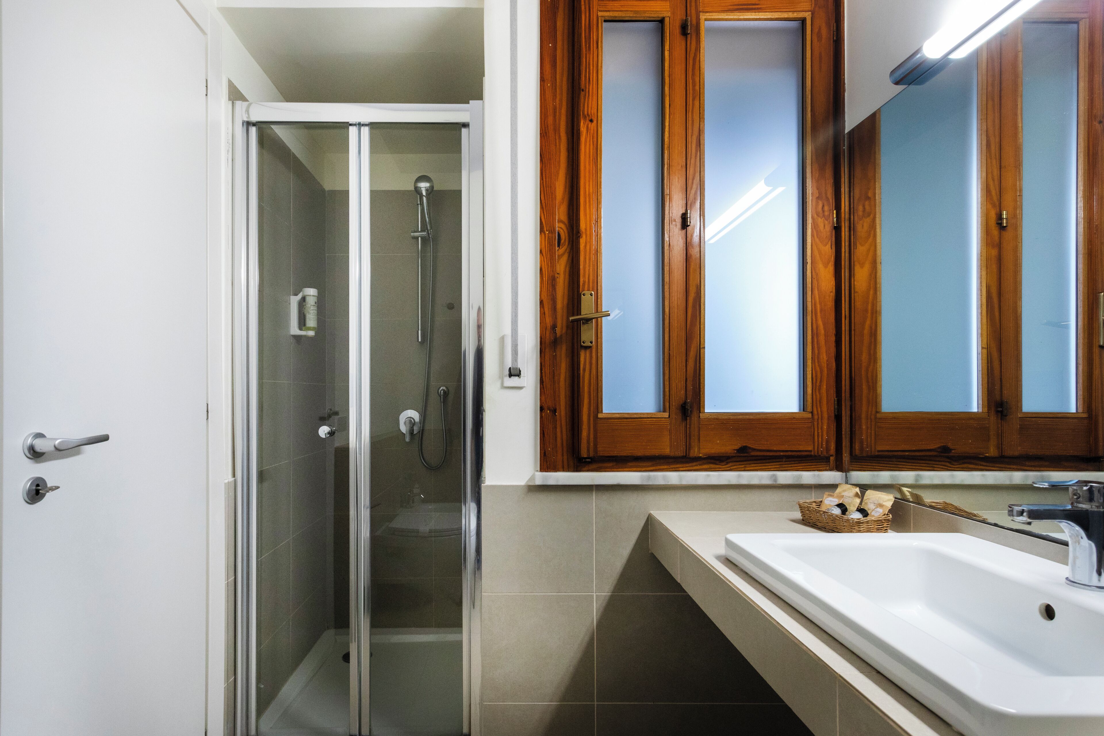 A bathroom with a glass-enclosed shower, a wooden vanity with a mirror, and a sink.