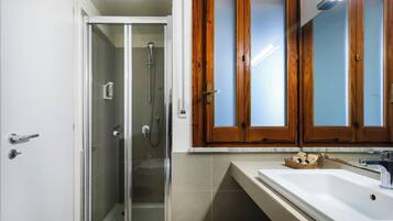 A bathroom with a glass-enclosed shower, a wooden vanity with a mirror, and a sink.