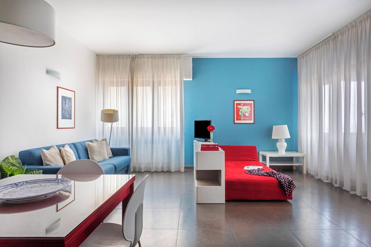 A modern living room with a blue accent wall, a red sofa, a white coffee table, and a TV stand.