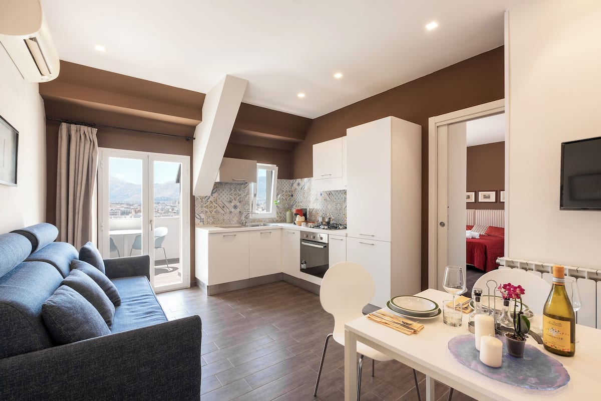 A modern kitchen with white cabinets, a dining table set with plates, glasses, and a bottle of wine.
