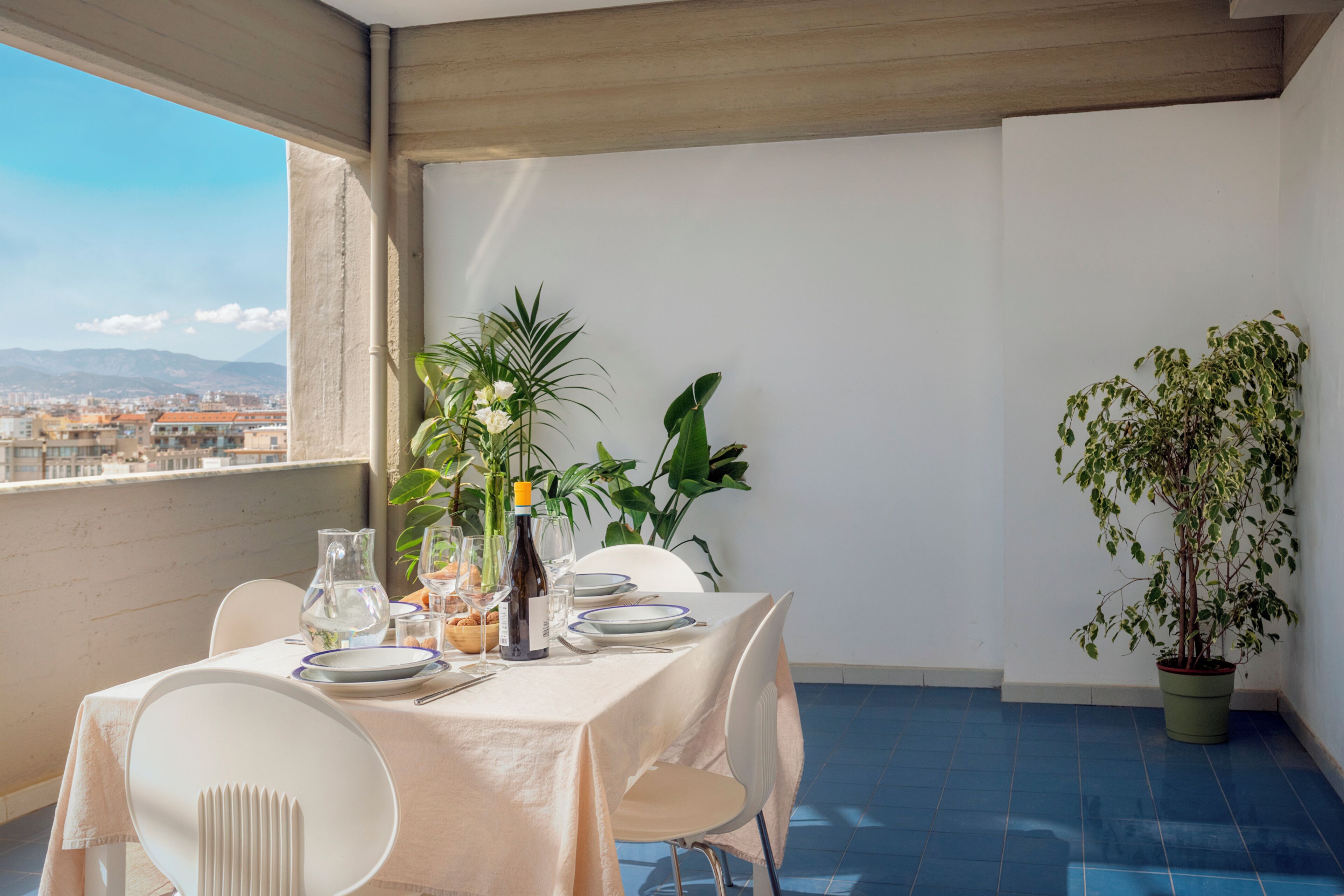 Un comedor con una mesa lista para dos personas, una planta en maceta y vistas de la ciudad.