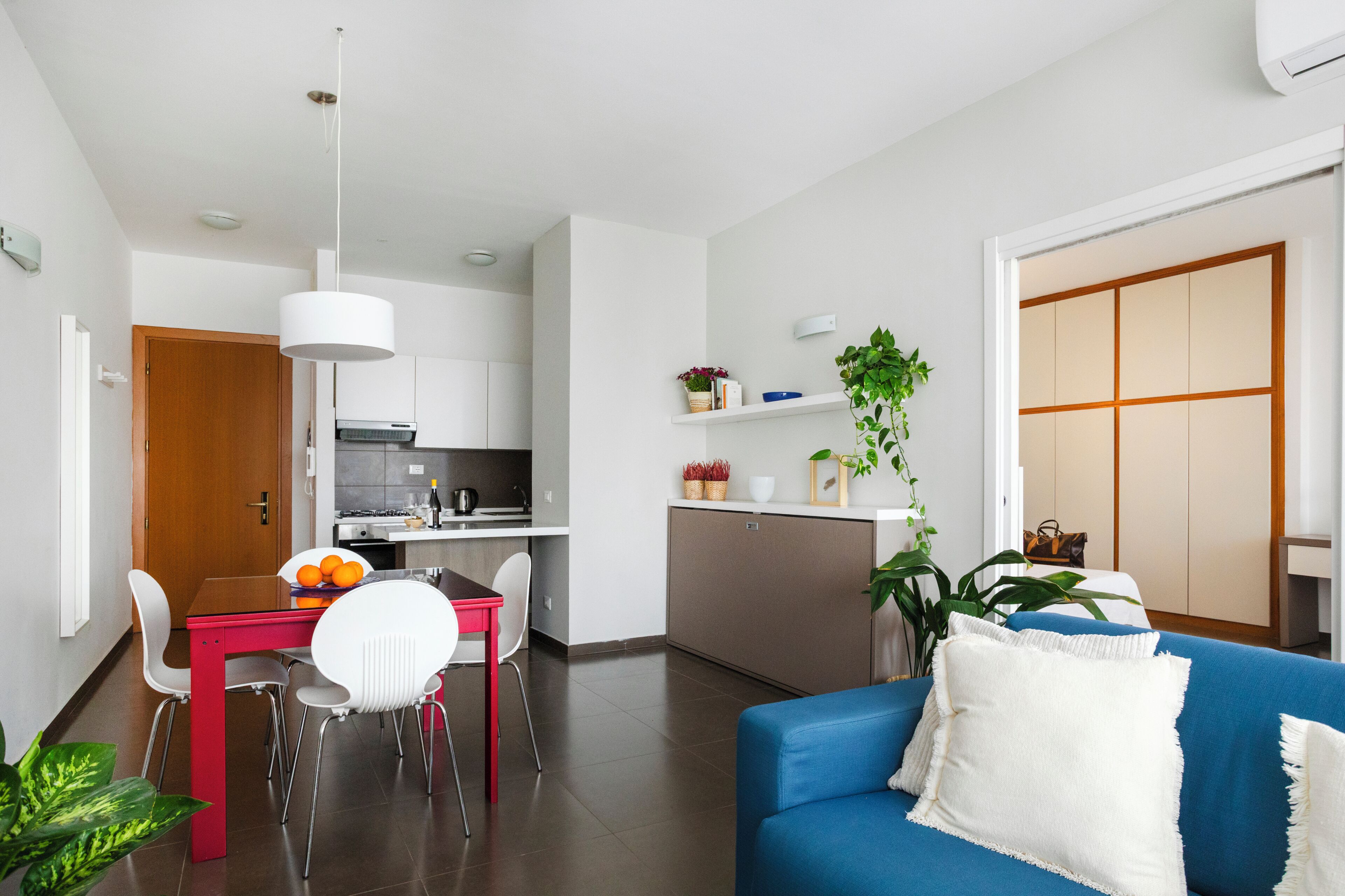 A modern living space with a dining area, kitchen, and a blue sofa with a white pillow.