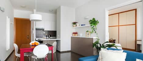 A modern living space with a dining area, kitchen, and a blue sofa with a white pillow.