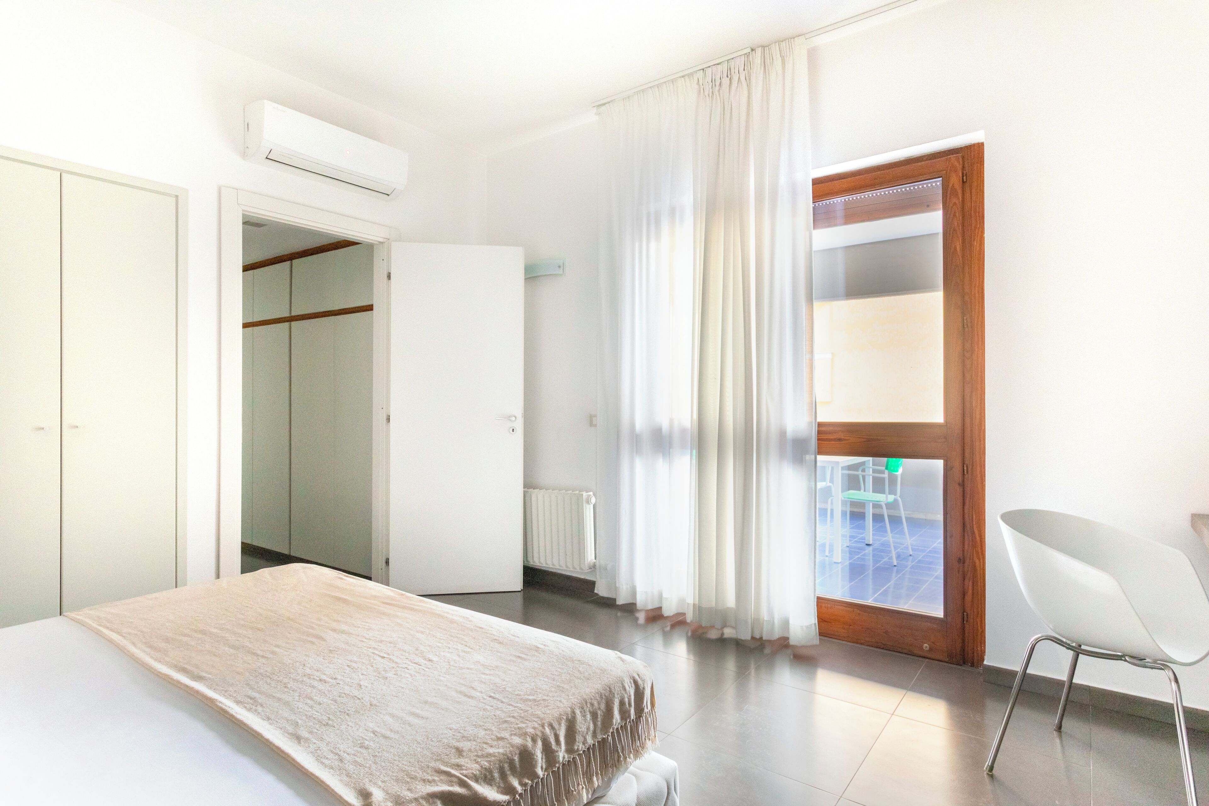 Ein Schlafzimmer mit Bett, Stuhl, Kleiderschrank, Tür und einem Fenster mit Vorhängen.