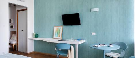 A modern hotel room with a bed, a desk with a chair, a TV mounted on the wall, and a small table with a chair.