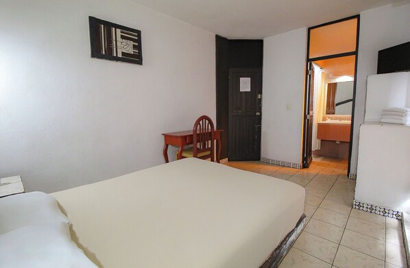 Una habitación con una cama, una silla, una puerta y una mesita.