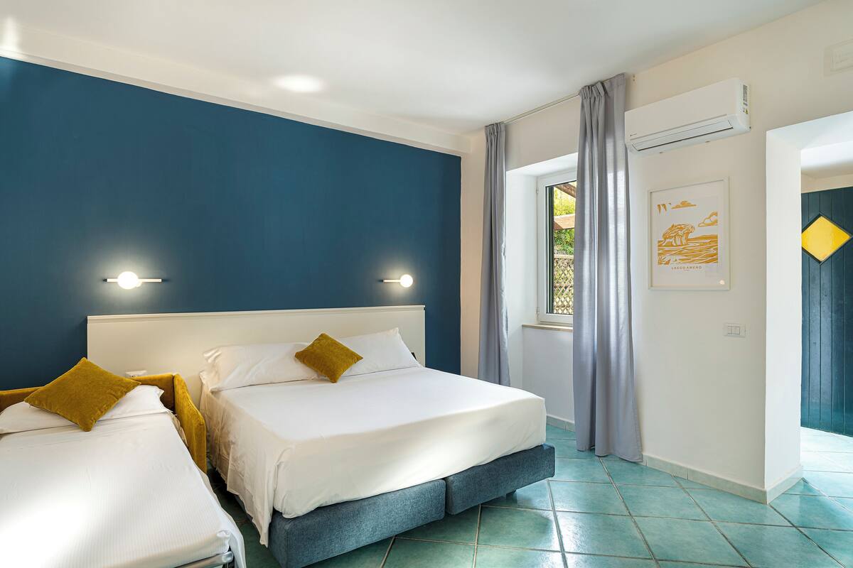 Una habitación de hotel con dos camas, un ventanal con cortinas y un equipo de aire acondicionado en la pared.