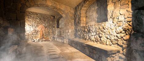 A stone-walled room with a central corridor and benches along the walls.