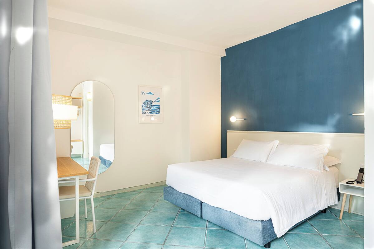 Un dormitorio con cama, un escritorio, una silla, un espejo y una lámpara fijada a la pared.