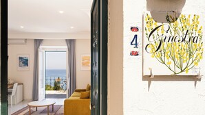 L’intérieur d’un hôtel, avec un canapé, une table et une vue sur la mer, visible à travers une porte vitrée.