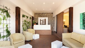 Un espace d’accueil comprenant un comptoir de réception en bois, un guichet d’enregistrement et un coin salon avec des canapés et des fauteuils à motifs.