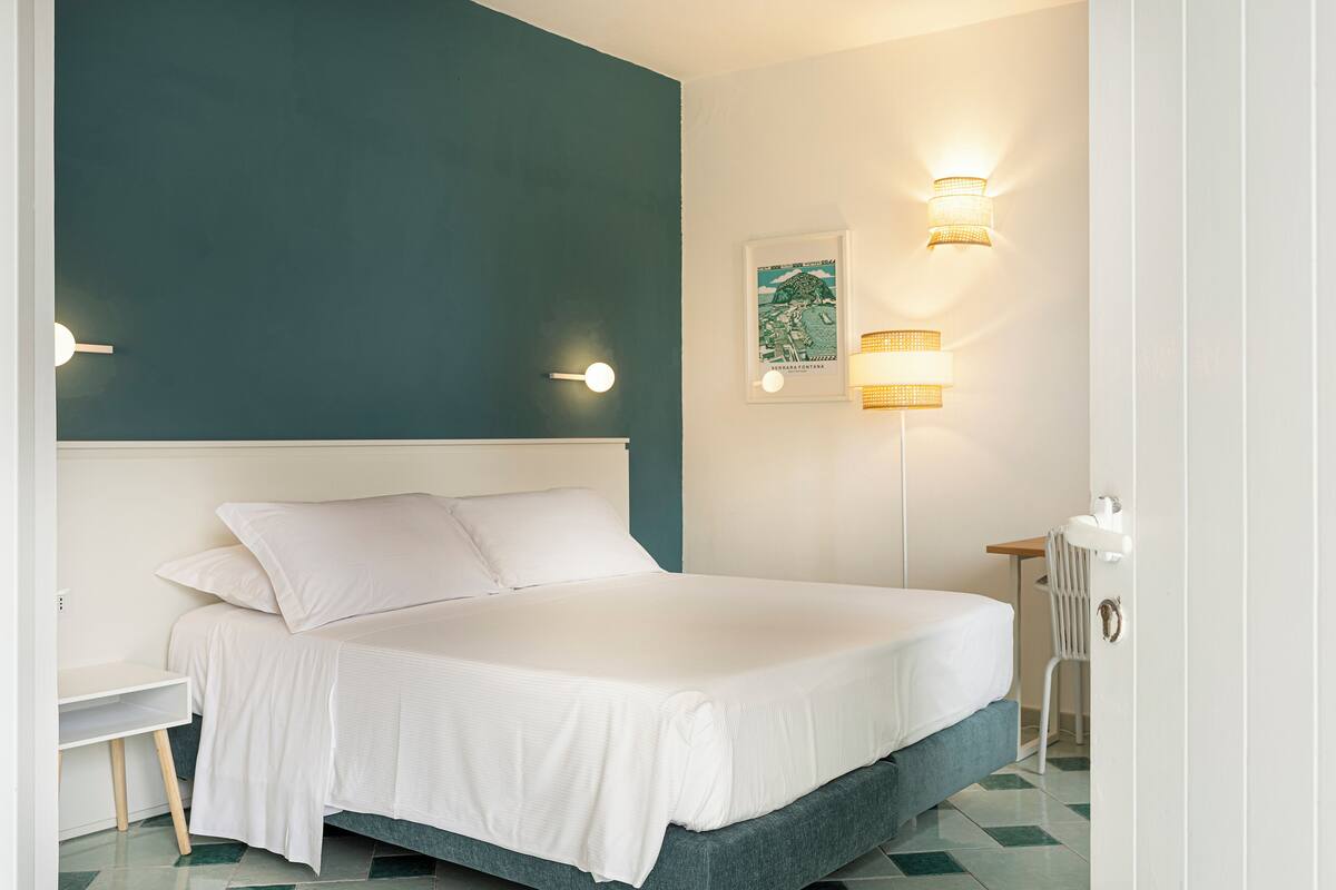 Un dormitorio con cama, mesita de noche y lámparas fijadas a la pared.