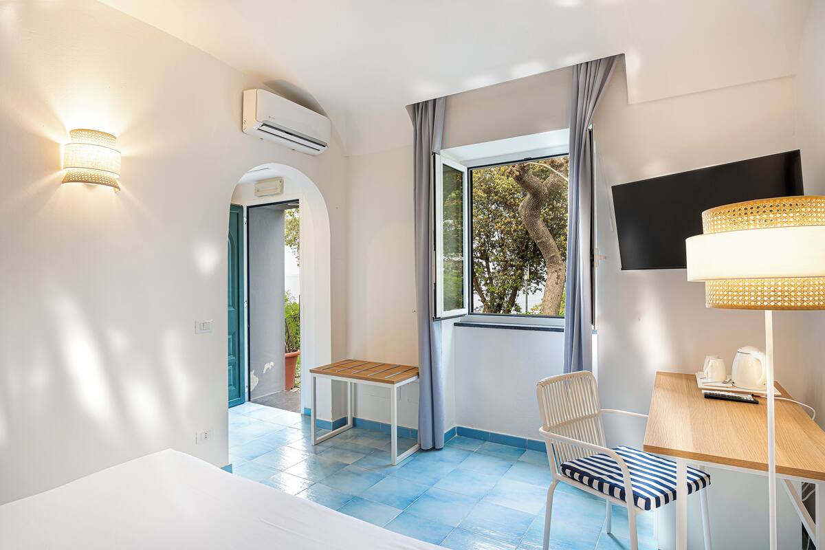 Una habitación con cama, una mesa con silla, televisión y ventana con cortinas.