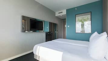 Una habitación de hotel con cama, televisor montado en la pared y un cuadro enmarcado.