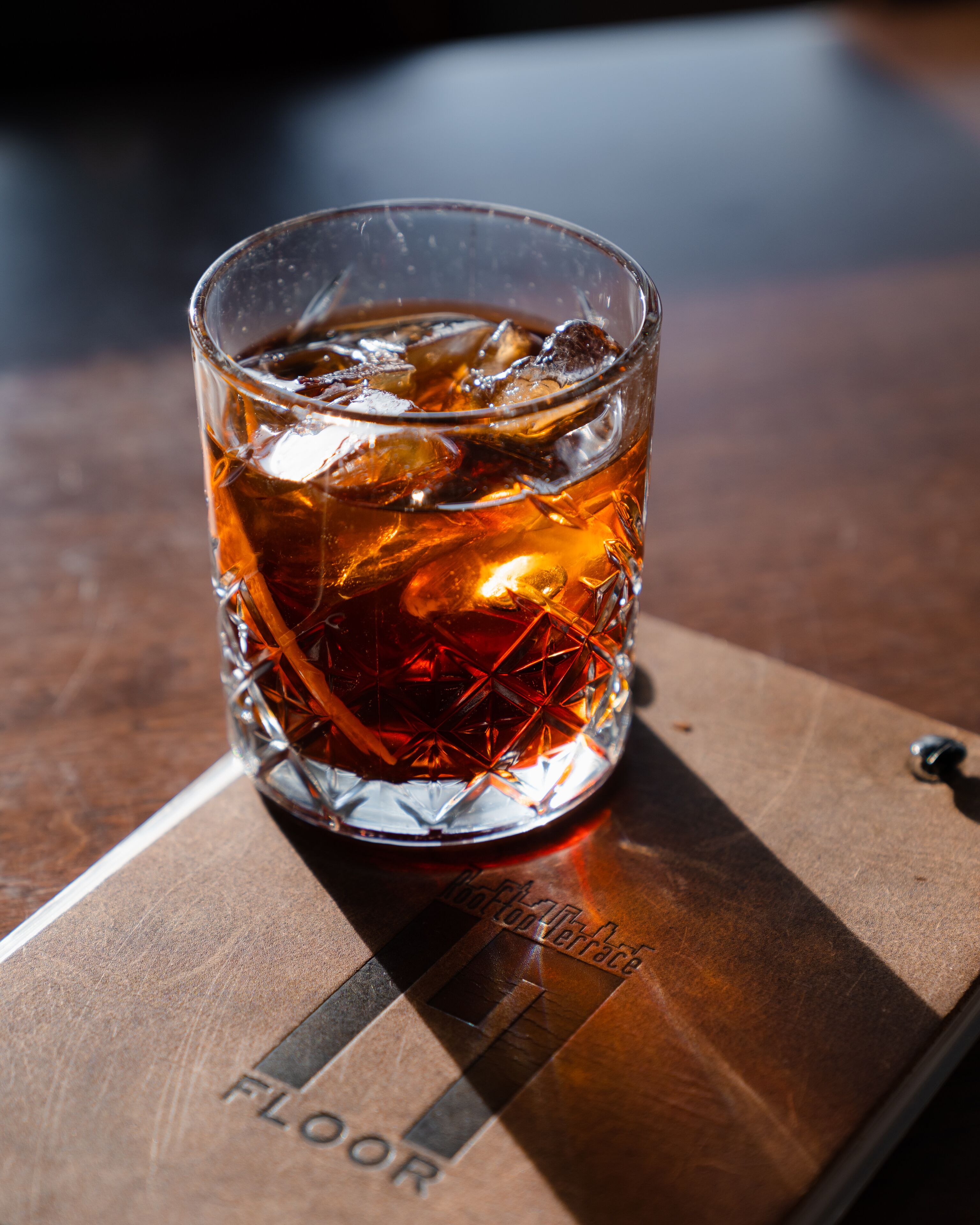 Un verre contenant un liquide ambré et quelques glaçons, posé sur un sous-verre en bois orné d’un texte en relief.