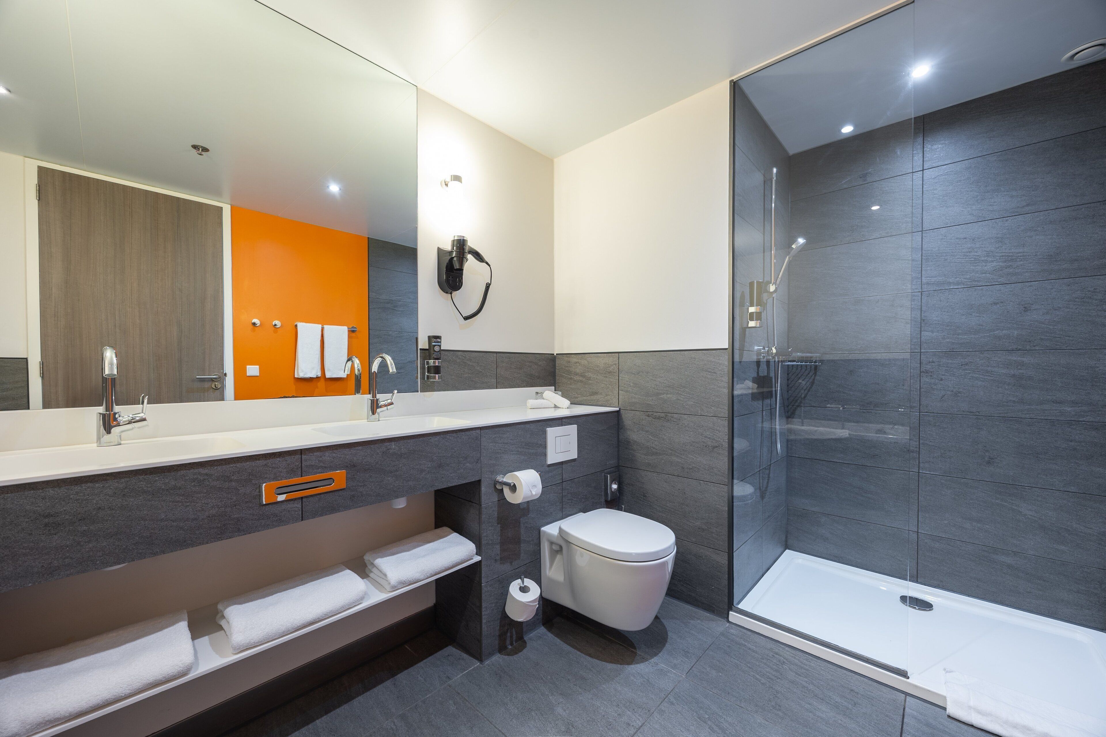 A modern bathroom with a large mirror, a shower enclosure, and a vanity with a towel rack.