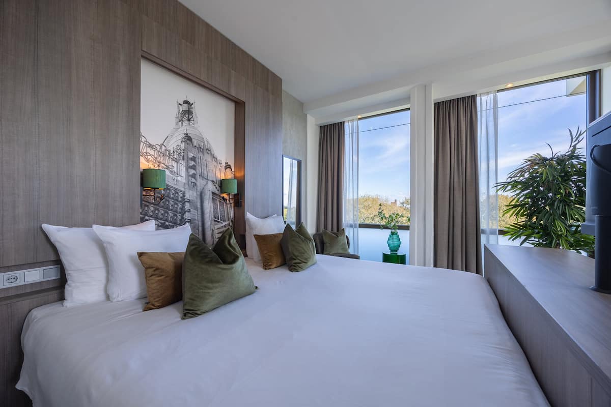 Ein modernes Hotelzimmer mit einem großen Bett, Blick auf die Stadt und einem Bild an der Wand.