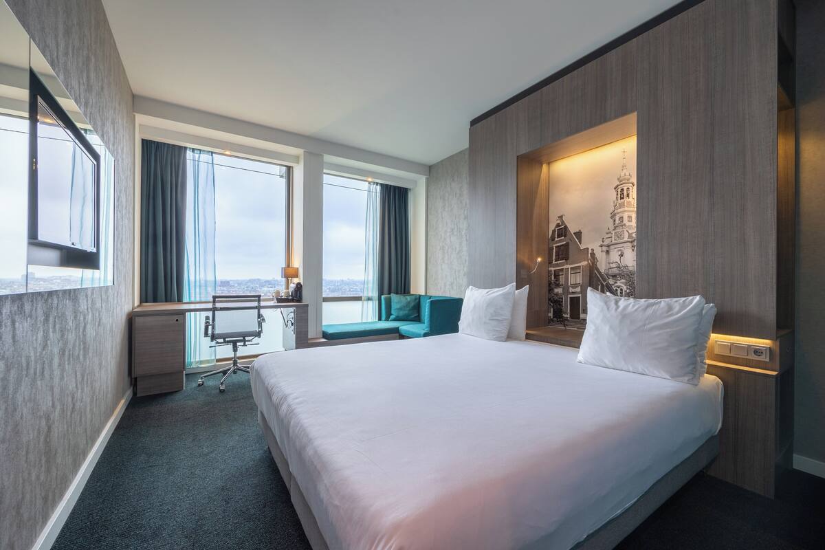 Ein Hotelzimmer mit einem großen Bett, einem Schreibtisch, einem Stuhl, einer Couch und Blick auf die Stadt.