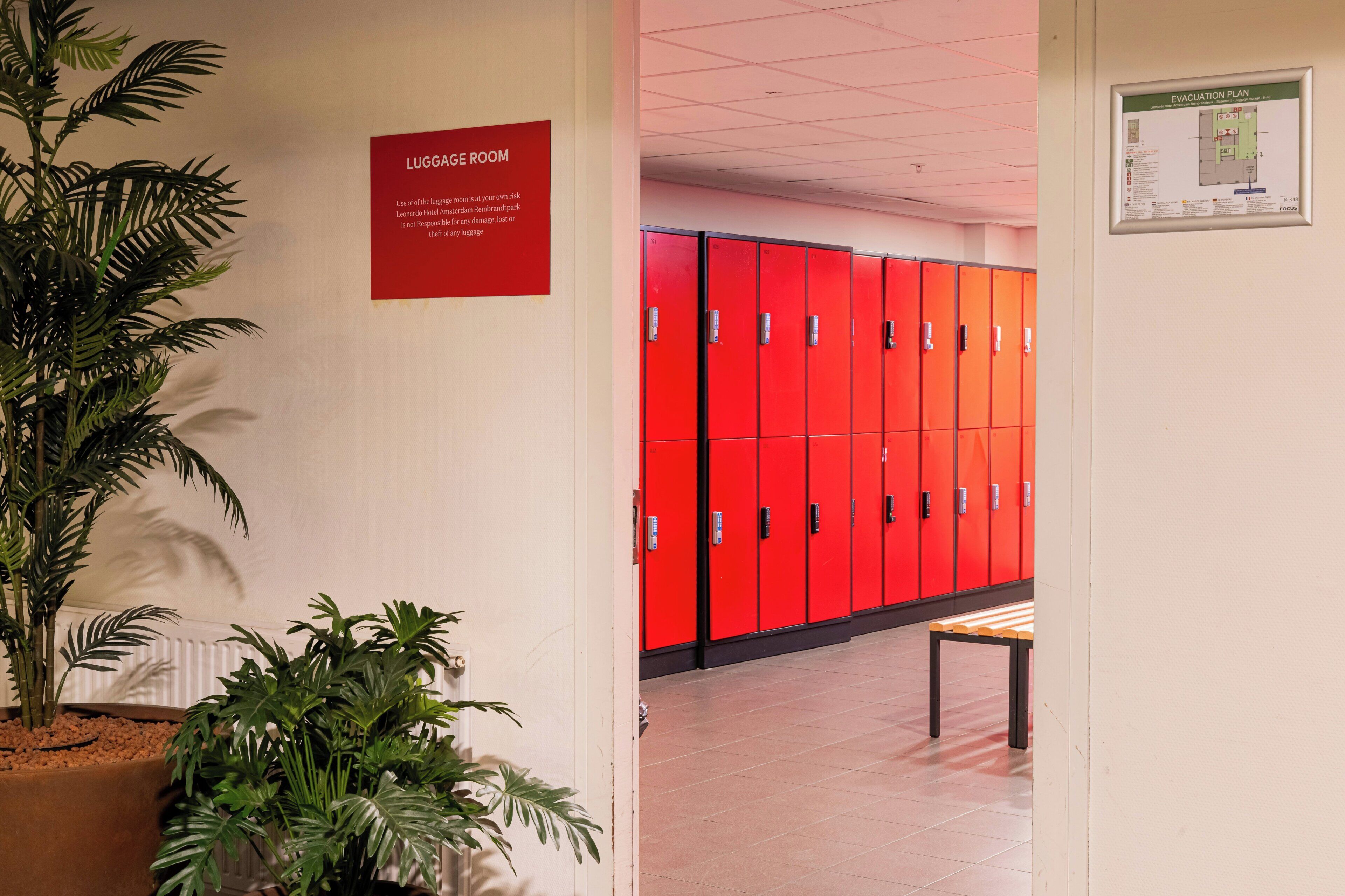 A hallway with red lockers, a luggage room sign, and an evacuation plan poster.