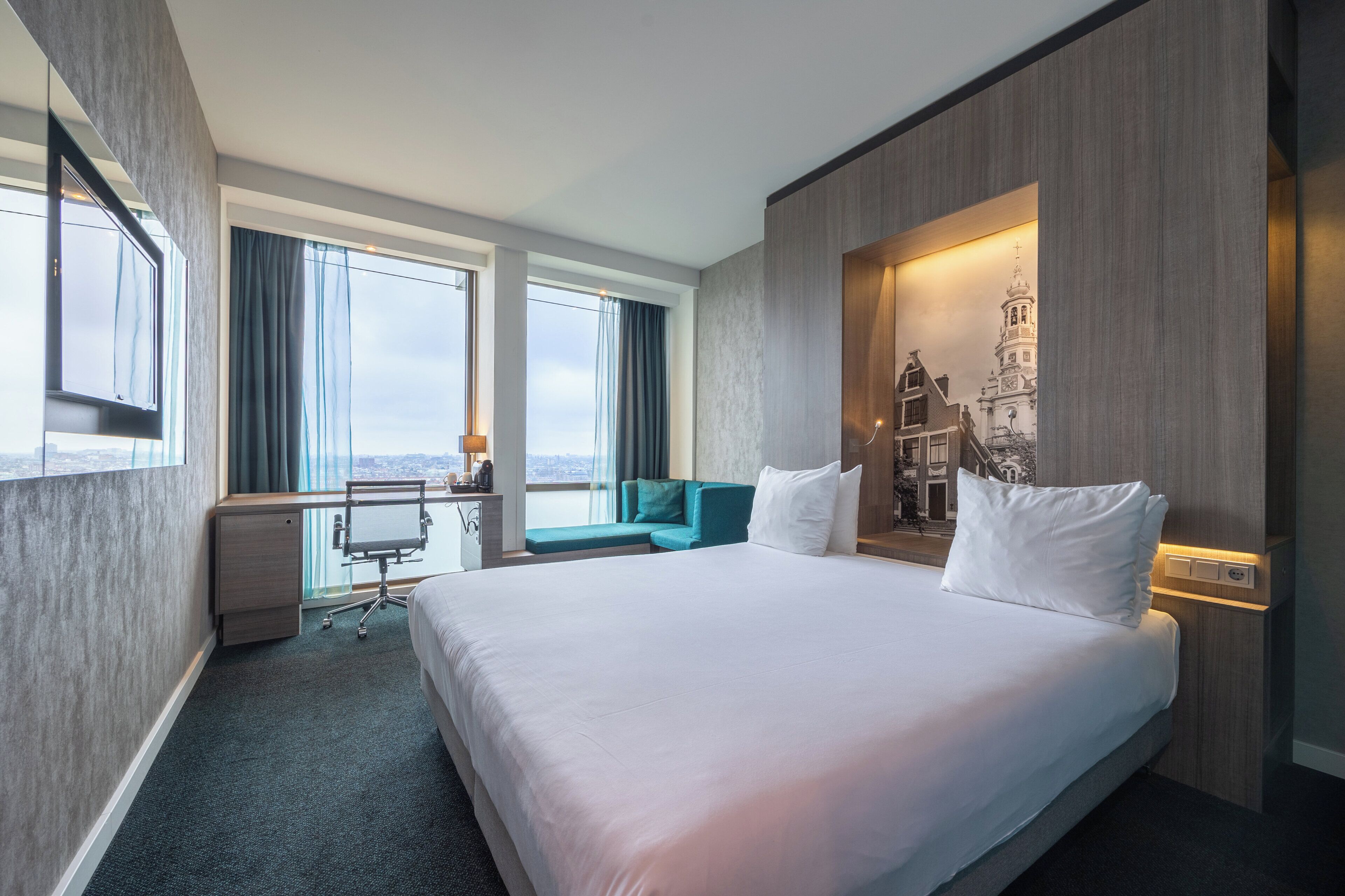 Ein Hotelzimmer mit einem großen Bett, einem Schreibtisch, einem Stuhl, einer Couch und Blick auf die Stadt.