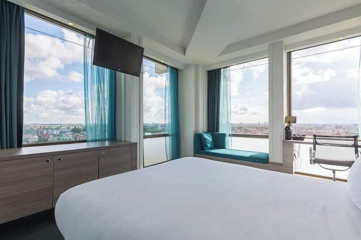 Ein Hotelzimmer mit einem großen Bett, einer Sitzecke mit Blick und einem an der Wand montierten Fernseher.
