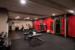 Une salle de sport équipée de matériel d’exercice, d’un tapis de course et d’un mur rouge.