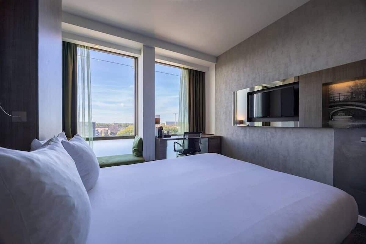 Ein modernes Hotelzimmer mit einem großen Bett, einem Schreibtisch, einem Flachbildfernseher und Blick auf die Stadt.