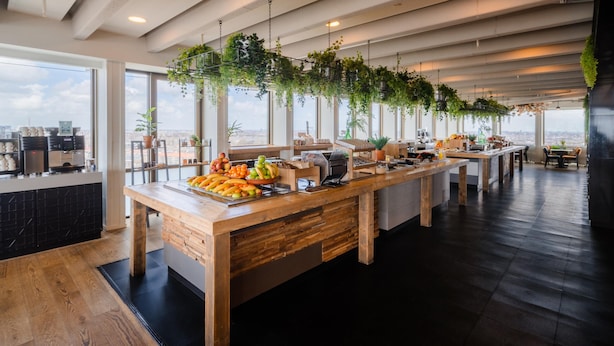 Una cocina moderna con una encimera de madera larga, plantas colgantes y vistas a la ciudad a través de amplias ventanas.