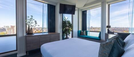 A hotel room with a large bed, a desk, a TV, and a view of the city.