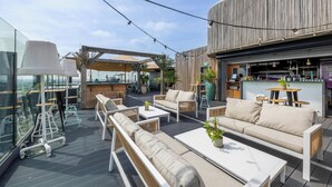 Una terraza en la azotea con mobiliario exterior, una zona de bar y vistas del horizonte de la ciudad.