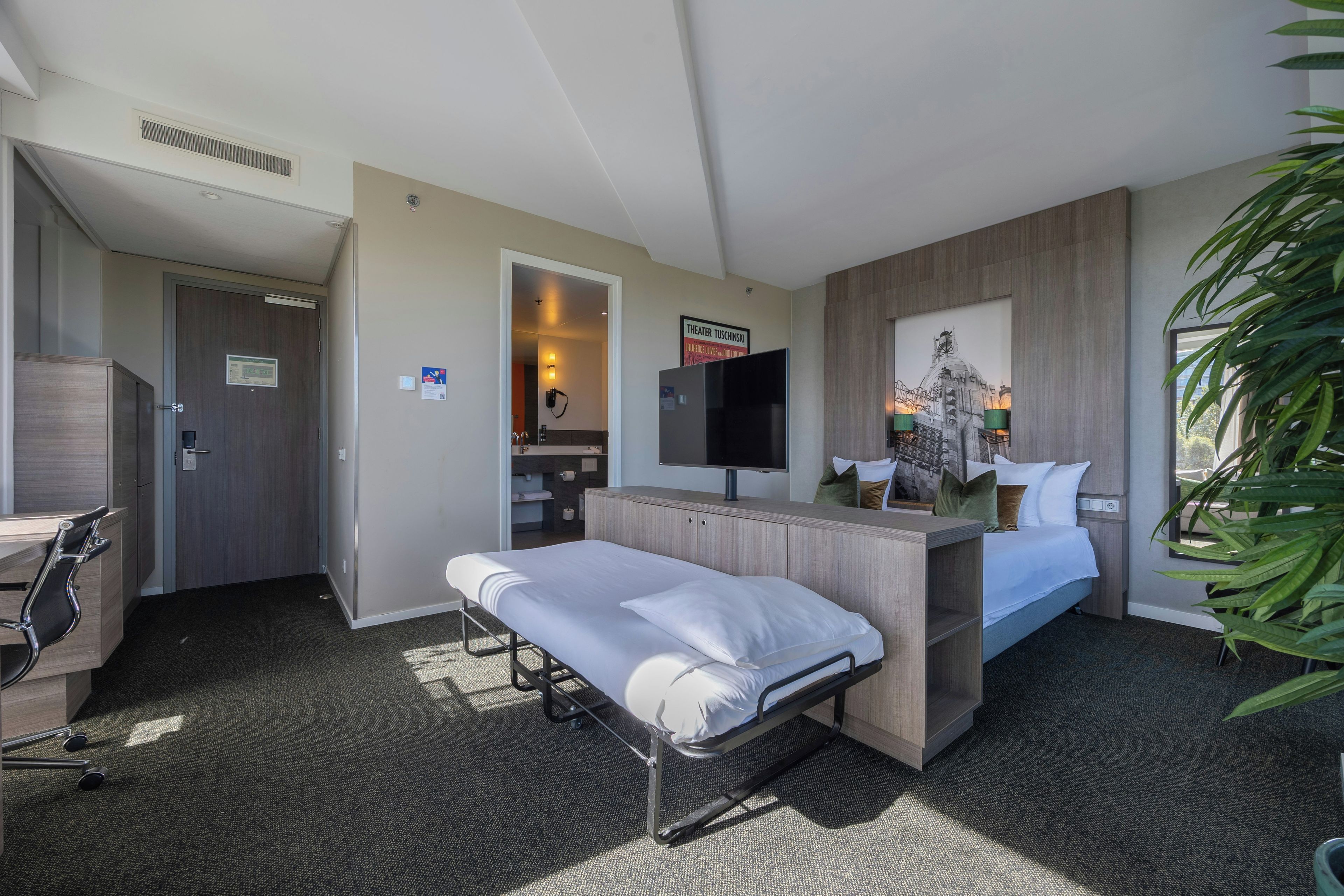 Une chambre d’hôtel avec un lit, un bureau, une chaise, une télévision et une grande fenêtre.