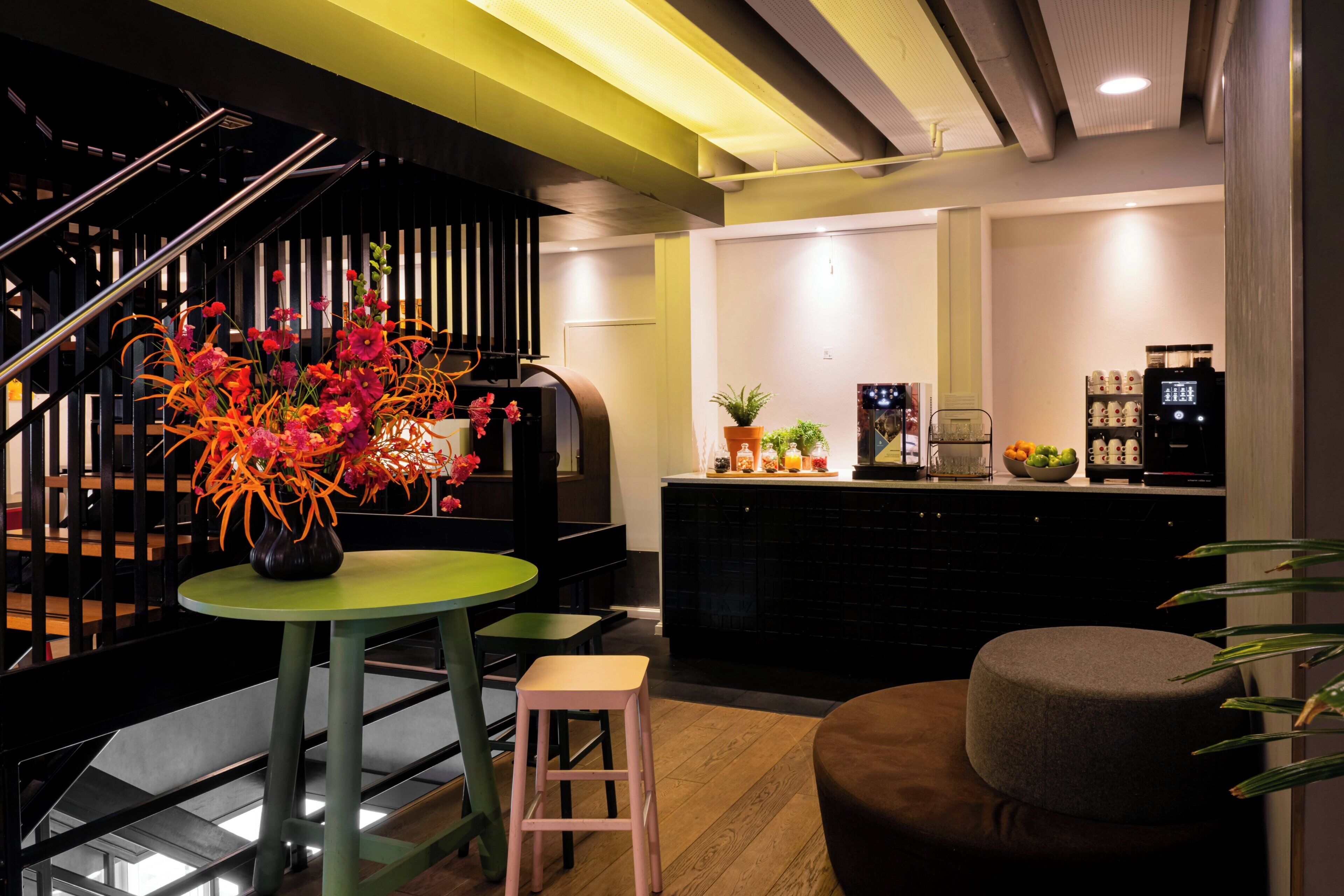Un interior moderno con una escalera, una mesa verde con un florero, una zona de cocina con electrodomésticos y un espacio de estar.