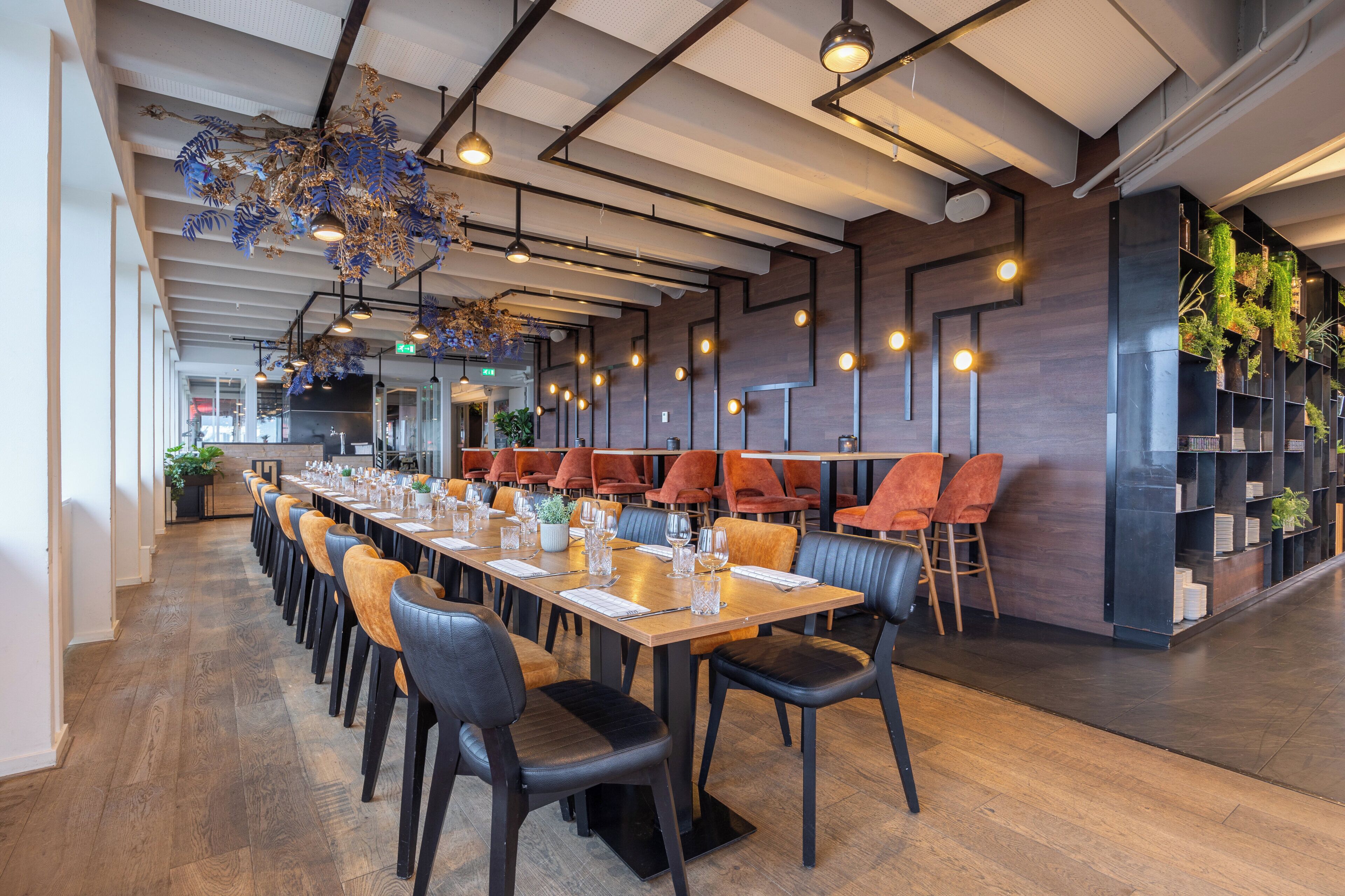 A modern restaurant with long communal tables, leather chairs, and hanging blue decorative elements.