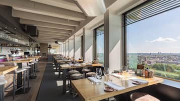 Ein modernes Restaurant mit langen Tischen und einer Bar, große Fenster mit Blick auf die Stadt.