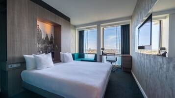 Ein modernes Hotelzimmer mit einem großen Bett, einem Schreibtisch und Blick auf eine Skyline.