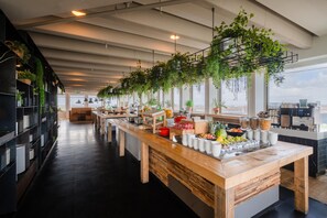 Un buffet moderne, avec un long comptoir en bois, une variété de plats et des plantes suspendues.
