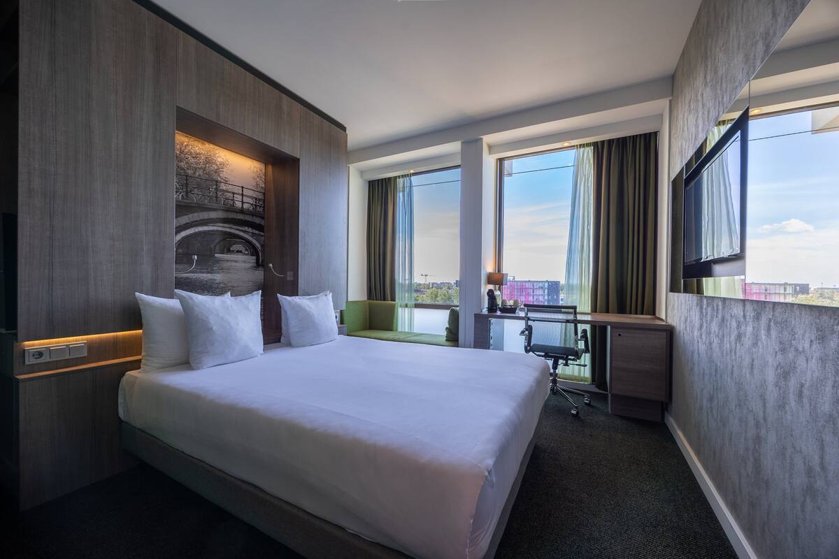 Ein Hotelzimmer mit einem großen Bett, einem Schreibtisch und Blick auf eine Brücke und die Stadtlandschaft.