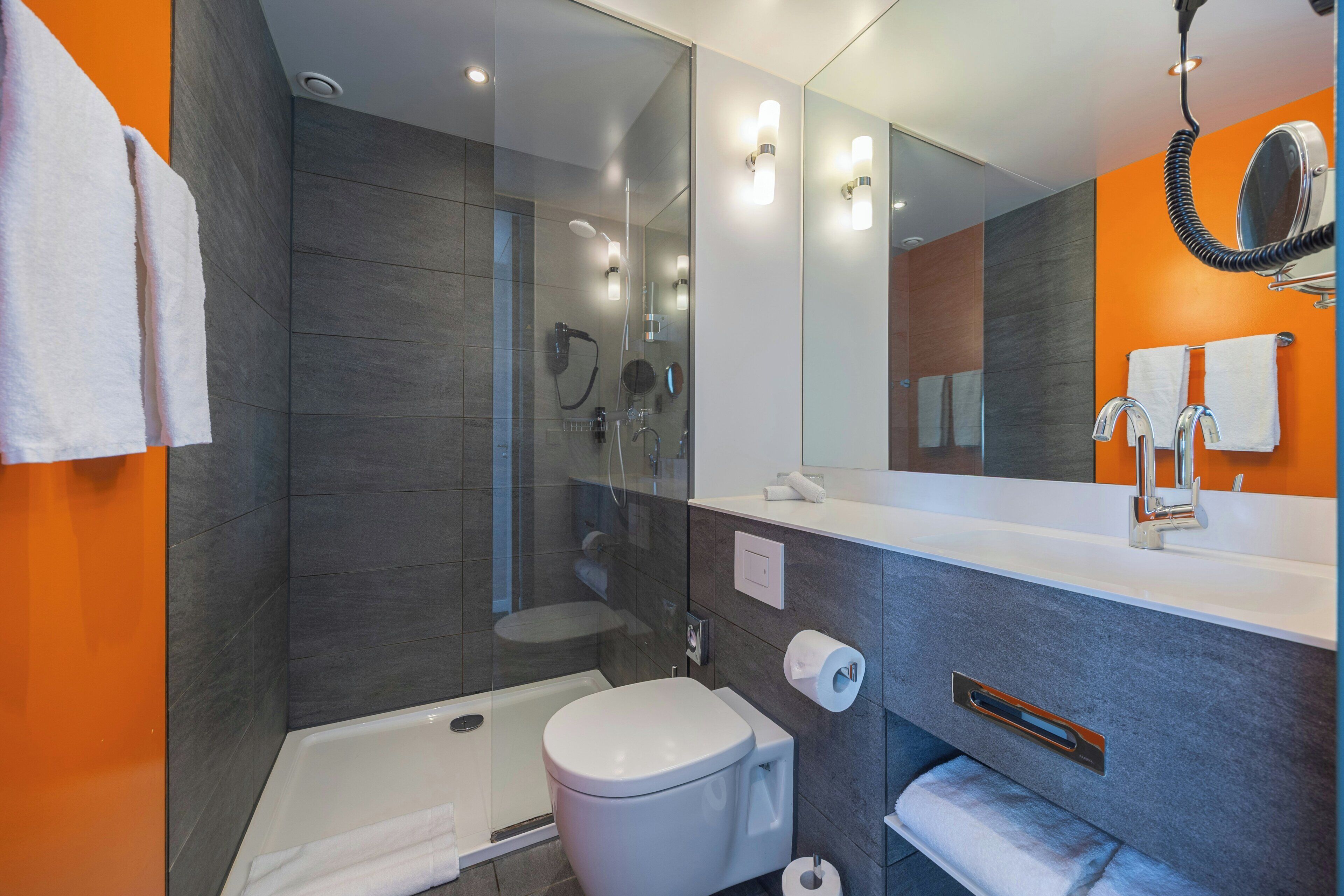 A modern bathroom with a glass-enclosed shower, a white toilet, and a vanity with a mirror.