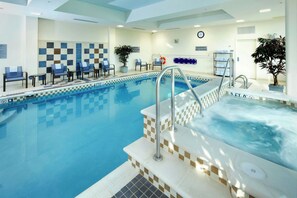 Una piscina interior con un jacuzzi, sillas de descanso y un cartel de seguridad.