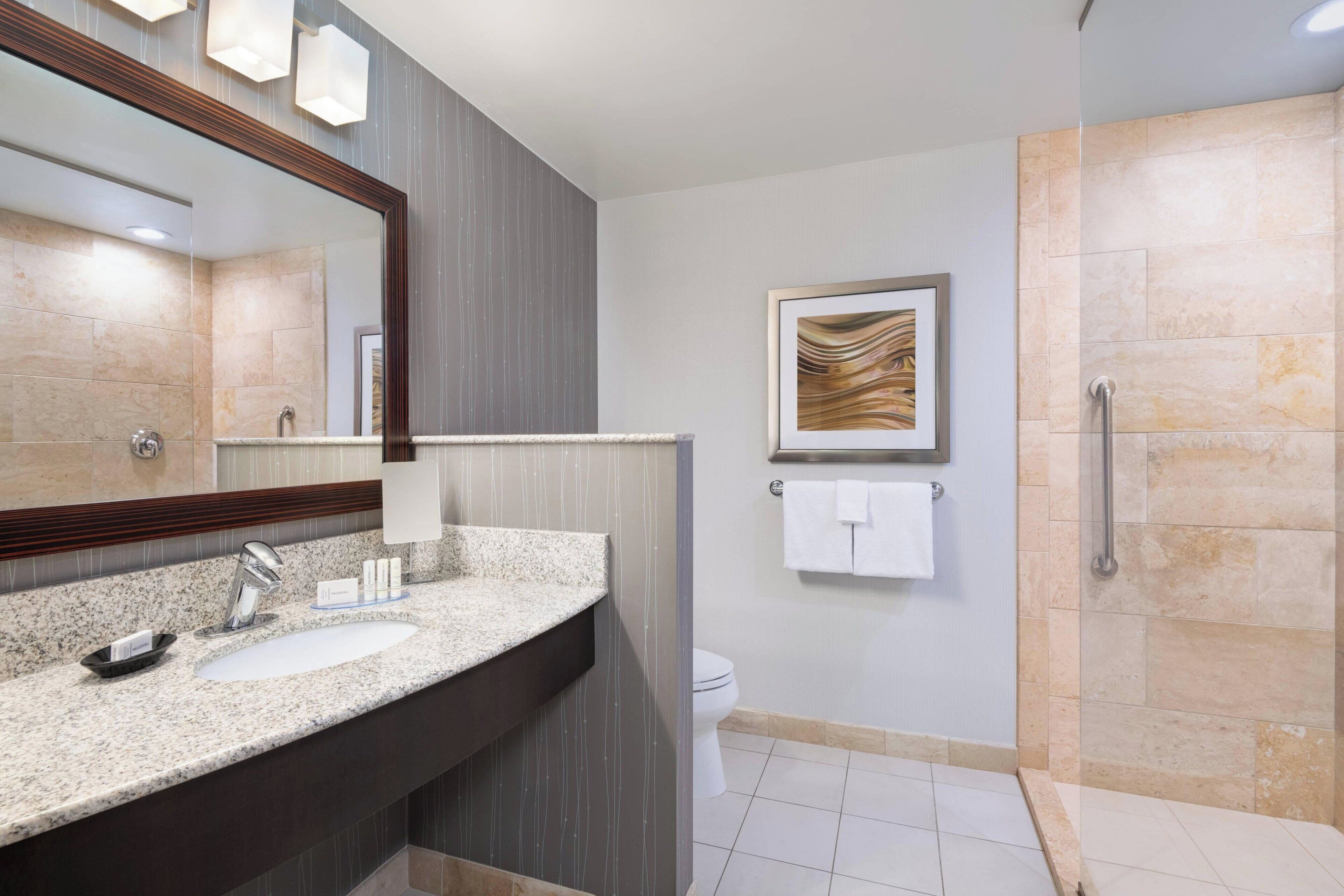A modern bathroom with two sinks, a large mirror, a shower area, and a framed artwork on the wall.