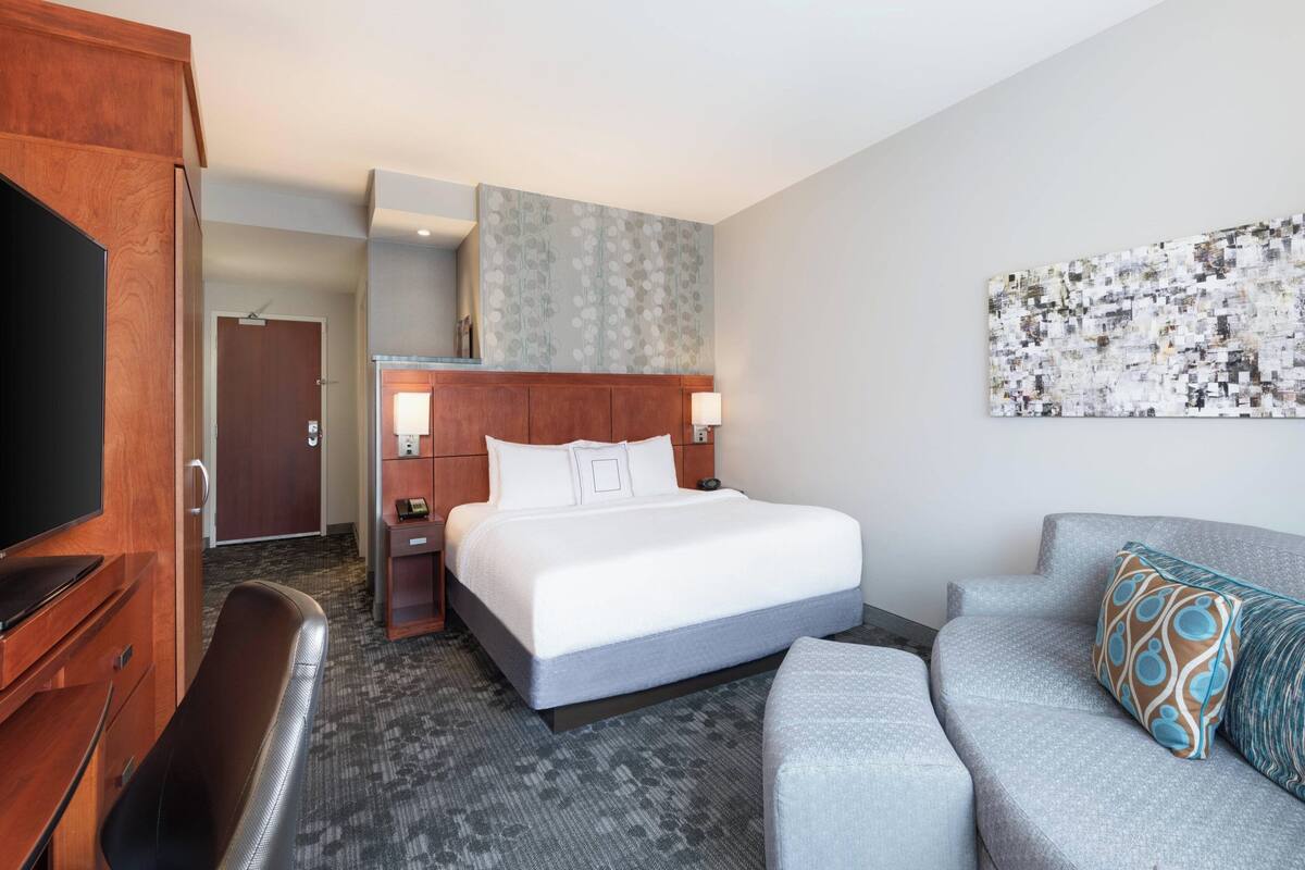 Une chambre d’hôtel équipée d’un lit, d’un bureau, d’une chaise, d’un canapé et d’un téléviseur fixé au mur.
